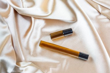 İpek kumaşın kıvrımlarında duran koyu camdan yapılmış kozmetik ürünleri depolamak için bir kap.