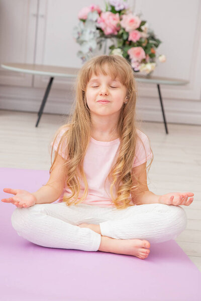 Симпатичная игривая девочка дошкольного возраста в полный рост выполняет различные упражнения. Счастливая девушка, практикующая йогу дома.