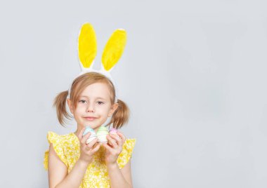 Tavşan kulaklı ve gri bir arka planda Paskalya için süslemeleri olan beyaz bir kızın portresi. Metin eklenecek yer ile paskalya arkaplanı.