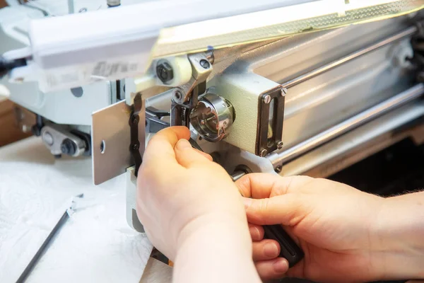 Female hands with a screwdriver repair the shuttle of the sewing machine. Repair of an industrial sewing machine at home. Maintenance.
