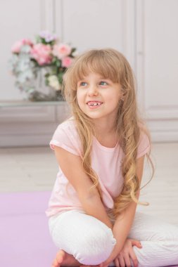 Yoga minderinde oturan sevimli, oynak, anaokulu kızı. Evde yoga yapan mutlu bir çocuk..