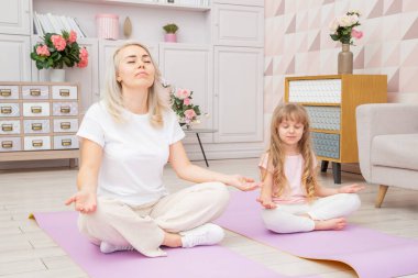 Yoga minderinde gülümseyen sarışın bir anne ve sevimli bir anaokulu kızıyla birlikte çeşitli egzersizler yapıyorlar. Mutlu anne küçük çocukla yoga yapıyor..