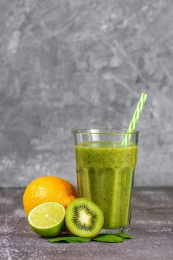 Gri beton arka planda meyvelerle çevrili uzun bir bardakta taze, sağlıklı meyve suyu. Uygun beslenme, kilo kaybı, vücudun zehirlenmesinden arınması..
