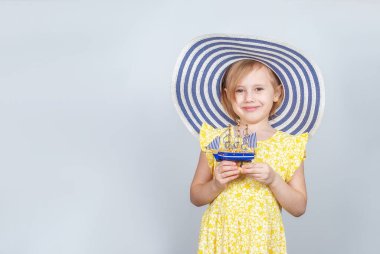 Geniş kenarlı şapkalı beyaz bir kız elinde oyuncak bir tekne tutuyor. Yaz tatili, seyahat, sahil sezonunun açılışı..