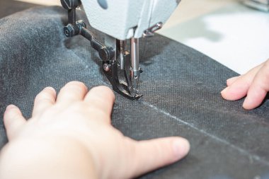 Bir kadın terzi endüstriyel dikiş makinesine siyah bir bez dikiyor.