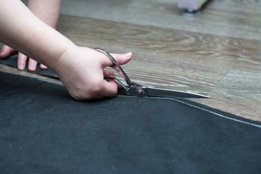 Kadının eli, evin zemininde siyah kaplama malzemesini makasla kesiyor.