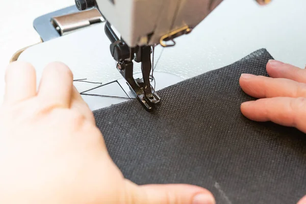 Bir kadın terzi endüstriyel dikiş makinesine siyah bir bez dikiyor.