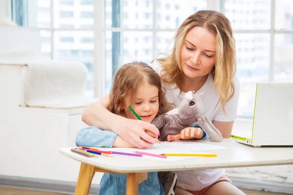 Happy Caucasian Mom With Daughter Sitting On The Living Room Floor And Drawing Together, Spending Time With Their Family Doing Art