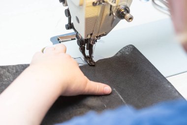 Bir kadın terzi endüstriyel dikiş makinesine siyah bir bez dikiyor.