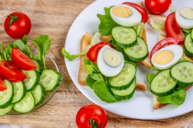 Kızarmış ekmek tostları, sebze ve yumurta dilimleri, salatalık ve domates salatası, ahşap bir arka planda.