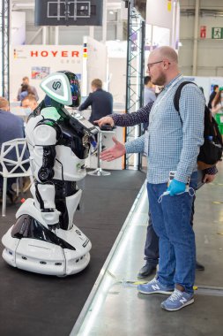 Moskova, Rusya - 14 Nisan 2021: Uluslararası ulaşım ve lojistik hizmetleri sergisinin tribünlerinden birinde bir sergi ziyaretçisi akıllı bir robotla el sıkışıyor