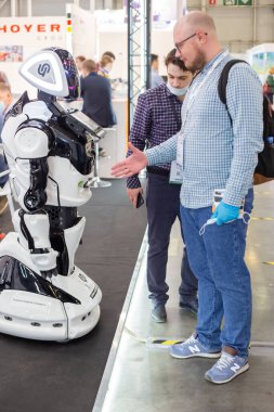 Moskova, Rusya - 14 Nisan 2021: Uluslararası ulaşım ve lojistik hizmetleri sergisinin tribünlerinden birinde bir sergi ziyaretçisi akıllı bir robotla el sıkışıyor