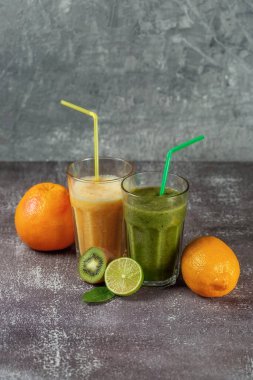 İki uzun bardak portakal suyu, muz-portakallı kivi ve gri beton arka planda meyve yarımlarıyla çevrili ıspanaklı içecek. Kilo verme ve düzgün beslenme kavramı.
