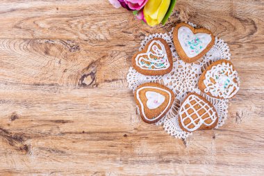 Dekoratif süslemelerle süslenmiş ev yapımı kalp şeklinde kurabiyeler, ahşap bir masada örülmüş bir peçeteye uzan, metin için yeri olan üst manzara.