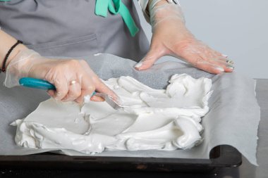 Kadın el şefi protein karışımını pişirme parşömeniyle kaplı yüzeyine yaydı. Pavlova Pastasının Pişirme Süreci.