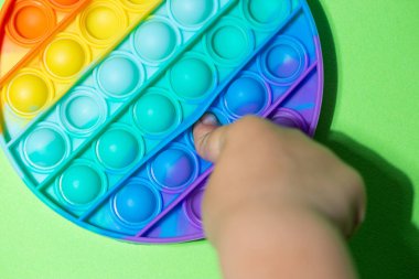 Beyazların çocukları duyusal anti-stres, çok renkli Pop It 'i yuvarlak şekilli oyuncakla oynarlar. Çocuklar ve yeşil arka planda yetişkinler için renkli stres önleyici silikon sensörler oyuncakları.
