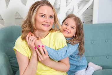 Küçük beyaz kız annesiyle birlikte oturma odasındaki kanepede oturuyor ve kameraya gülümsüyor. Çocuklarla evde vakit geçirmek..