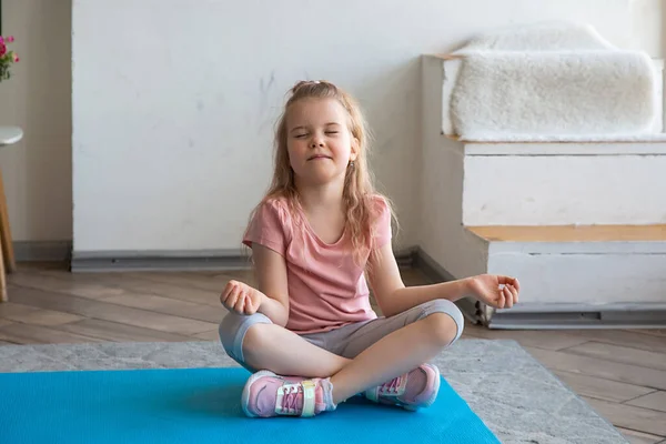 Portrait of little girl doing yoga sitting in lotus position on yoga mat — Stock Photo, Image