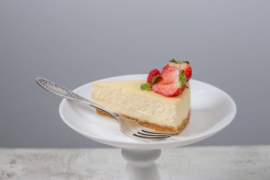 Beyaz bir zemin üzerinde beyaz bir tabakta çilekli cheesecake dilimi..
