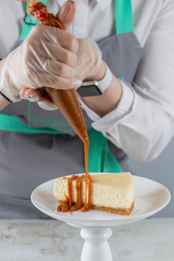 Pasta şefi beyaz tabakta en taze cheesecake dilimine karamel döker..