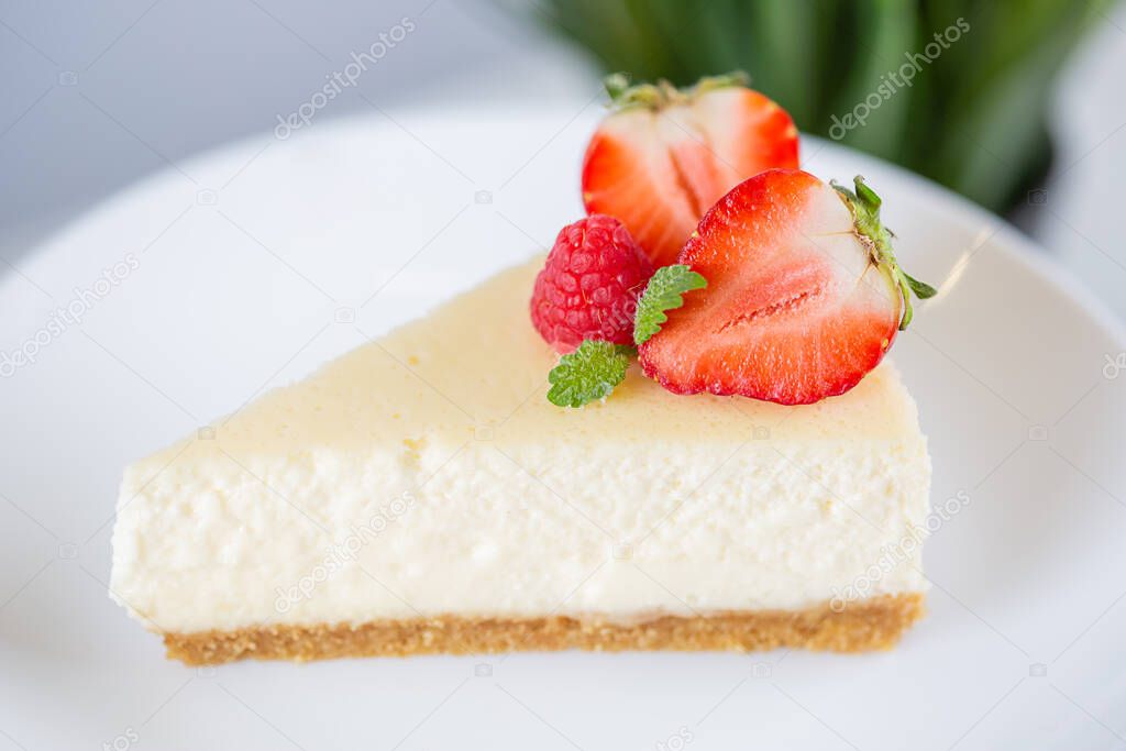 close-up of strawberry cheesecake on a white plate on a cake stand on a white background