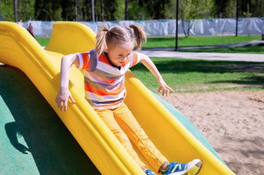Kafkasyalı küçük kız güneşli bir günde oyun parkında tepeden aşağı kayıyor..