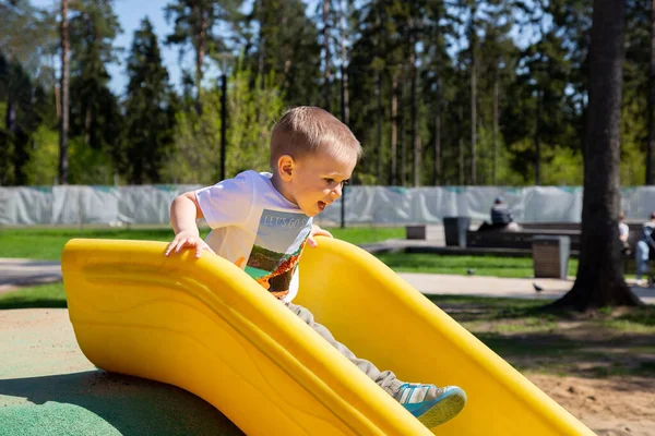 Kafkasyalı küçük çocuk oyun parkındaki tepeden aşağı kayıyor.