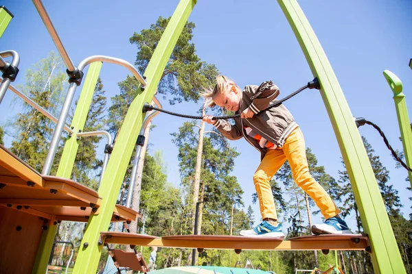 Liten flicka klättrar hängbro på lekplatsen utomhus — Stockfoto