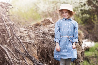 Ormanda kökleri ters dönmüş, devrilmiş bir ağacın yanında duran sevimli beyaz kız kameraya bakıyor.