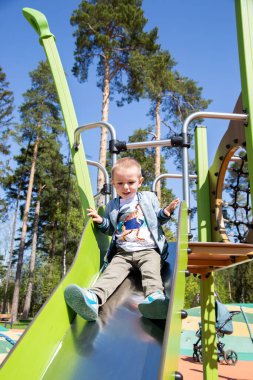 Kafkasyalı küçük çocuk güneşli bir günde oyun parkında tepeden aşağı kayıyor..