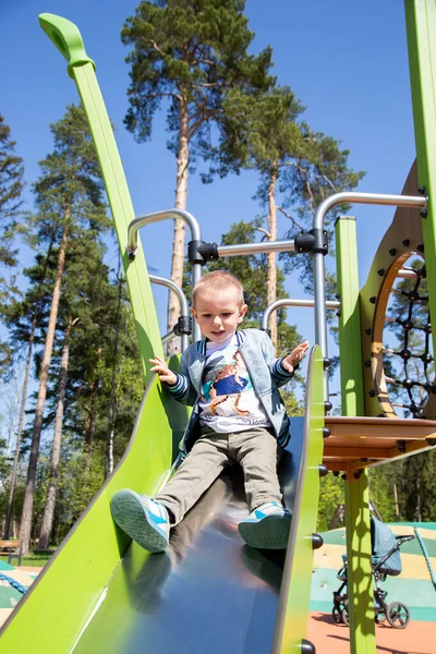 Caucasiano Menino Desliza Para Baixo Colina Playground Livre Dia Ensolarado — Fotografia de Stock