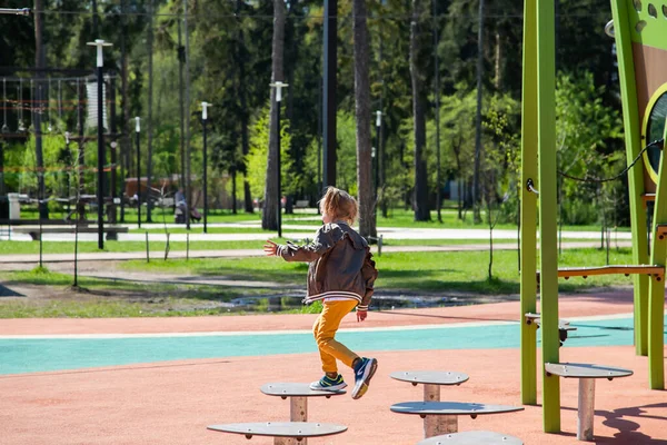 Liten flicka hoppar på simulatorn på hinderbanan i lekplatsen — Stockfoto