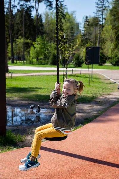 Caucásico niña monta un columpio bungee en el patio de recreo en un día soleado. — Foto de Stock