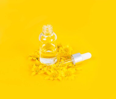 Sarı zemin üzerinde pipet serumu olan bir şişe. Etrafı bahar çiçekleriyle çevrili.