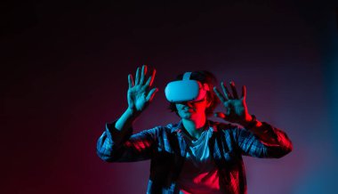 Beyaz kadın 35-40 yaş arası video gözlüklü, sanal gerçeklik kulaklığı takıyor, neon ışıklı bir şeye dokunmaya çalışıyor..