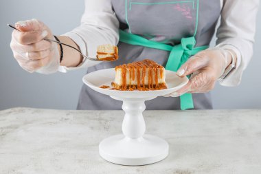 Bir pasta şefi beyaz bir tabakta çatalla karamel serpiştirilmiş en taze peynirli keki kırar.