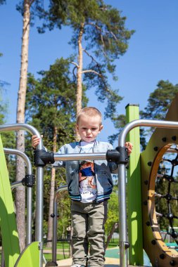 Kafkasyalı küçük çocuk güneşli bir günde oyun parkında kaymak için tek başına kayağa tırmanır..