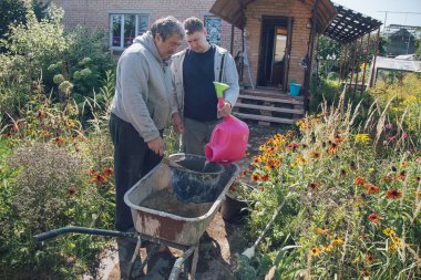 30 yaşındaki bir adam çimento karışımına su dökerek bahçeye çimento döker.