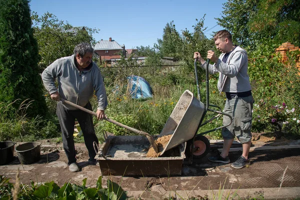 Bir adam çimento karışımına kum boşaltır bahçe yolu dökerek, bahçe arazisinde inşaat yapar.