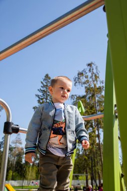 Kafkasyalı küçük çocuk güneşli bir günde oyun parkında kaymak için tek başına kayağa tırmanır..