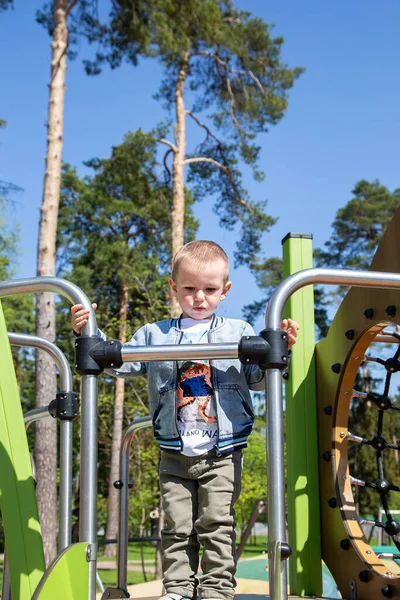 Kafkasyalı küçük çocuk güneşli bir günde oyun parkında kaymak için tek başına kayağa tırmanır..