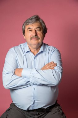 Pembe arka planda yaşlı bir adamın portresi kameraya bakıyor.