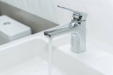 Modern kaplama havzası ve parlak paslanmaz çelik musluğu olan dikdörtgen beyaz mermer lavabo. Açık musluk akan su.