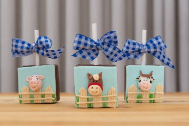 Kare çikolatalı lolipop çiftlik temalı. Çitin arkasında hayvan şeklinde badem ezmesi ile süslenmiş şeker. Domuz, at ve inek..