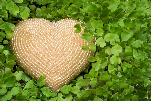 Beige beaded heart hidden in maidenhair fern. Love concept