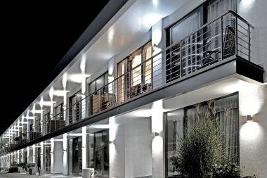 Geceleri ön cephesinde parlayan lambalar olan iki katlı modern bir bina.
