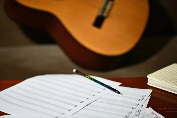 sheet music staves and a pencil lying on the table, with a classical guitar in the background