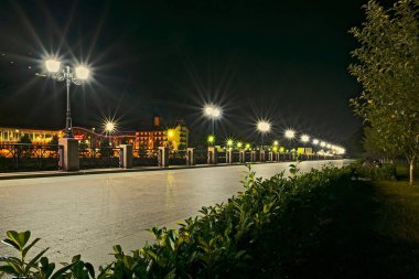 Aydınlatılmış bir gece şehrinde fenerli pürüzsüz fayanslardan yapılmış geniş kaldırımlar.