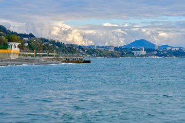 Bir dağ kasabasının arka planına karşı çakıl taşı plajında kubbeli bir pelerini olan deniz kıyısı.