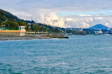 Bir dağ kasabasının arka planına karşı çakıl taşı plajında kubbeli bir pelerini olan deniz kıyısı.